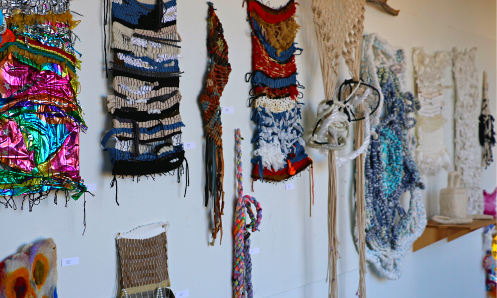 A weaving with bright-colored textiles from beginning fibers student hangs on the wall.
