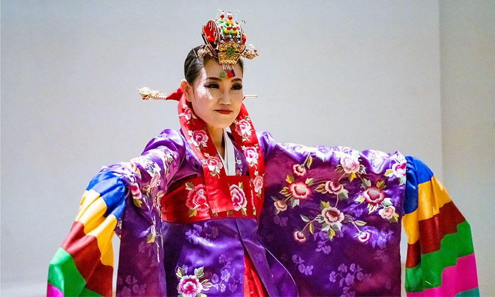 Kate Kim wears a brightly-colored hanbok and headdress while performing a traditional Korean prayer dance.