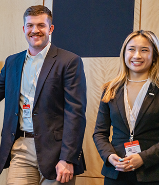 Two students in professional clothing stand at the front of a room.