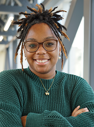 A portrait of Makaela Parker, a young Black woman wearing a green sweater.