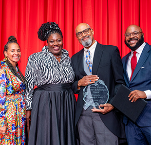 Four people stand together, one person holding a glass award.