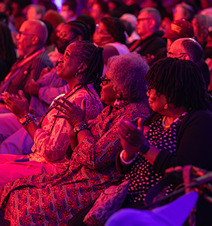 An audience, focused on three people in the middle, washed in red light.