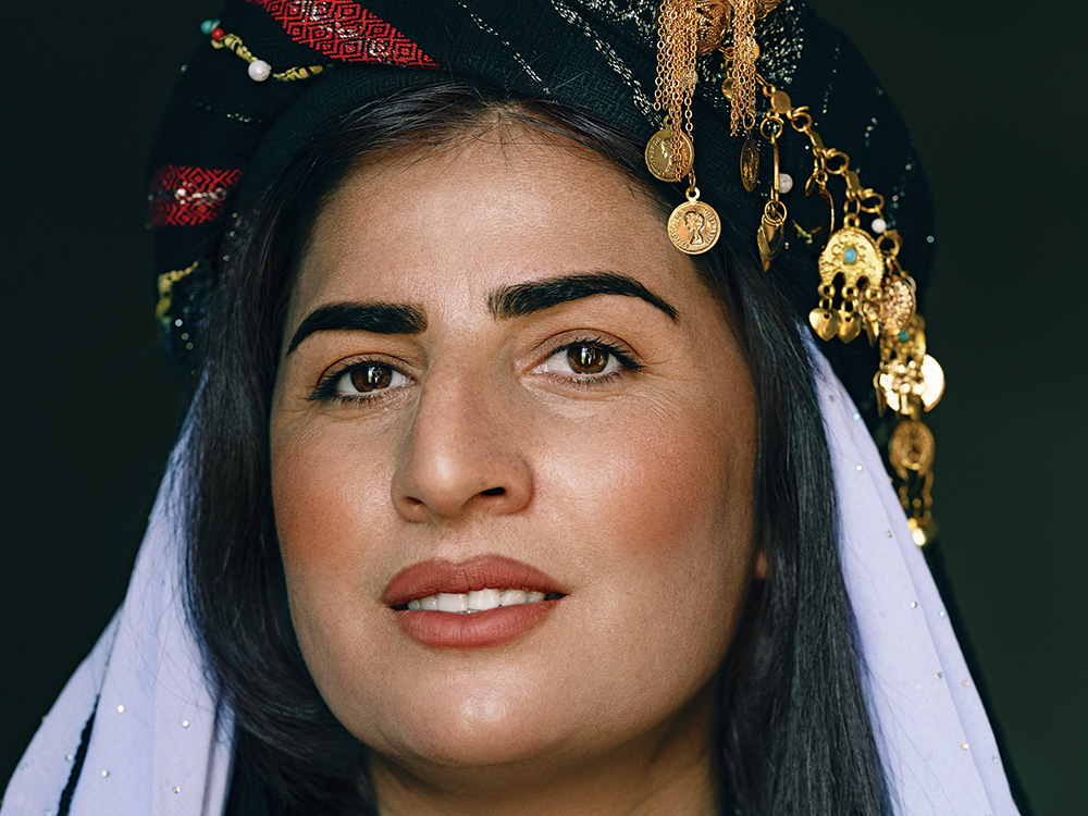A woman wearing a traditional headdress with patterned black and red cloth, adorned with gold jewelry.