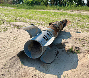A partially destroyed rocket on the ground by a treeline.