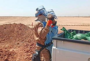 A man wearing blue personal protective equipment places an object in a truck bed.