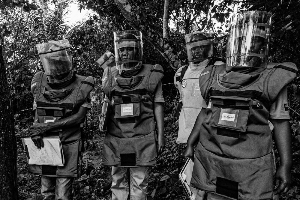 Four people standing side by side wearing protective clothing with clear masks and helmets.