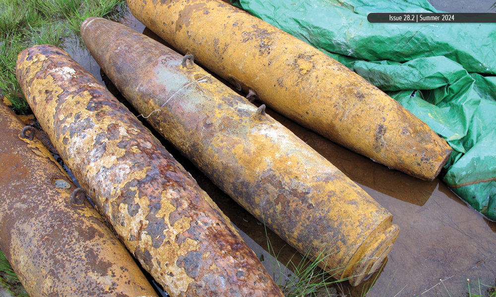 Three rusty munitions by a green tarp in shallow water.