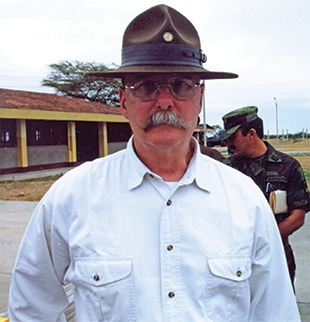 A man with a campaign hat, glasses, and moustache poses for a picture.