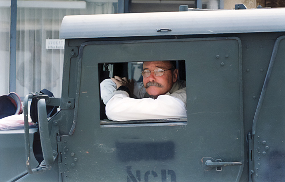 A man with glasses and a moustache inside a military truck.