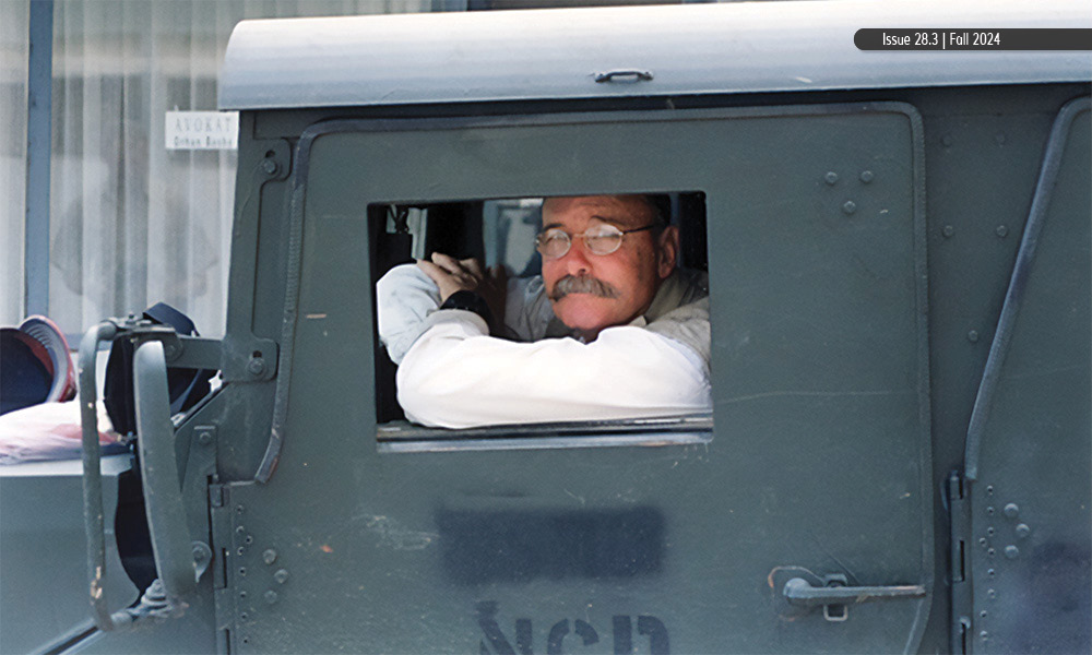 A man with glasses and a moustache inside a military truck.