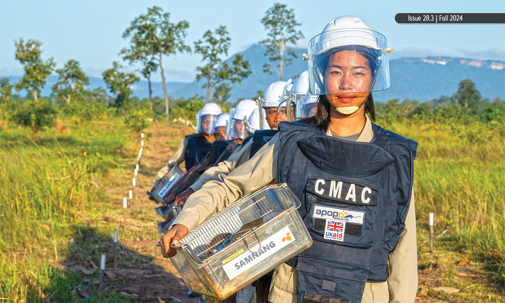 A column of people wearing protective aprons, helmets, and visors with trees and mountains behind them.