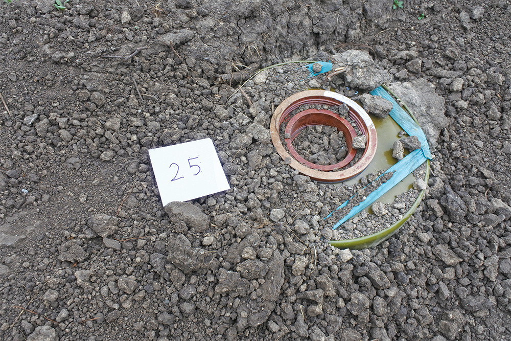 A circular object is partially buried in gravel next to a whit square pice of paper with the number 25 on it.