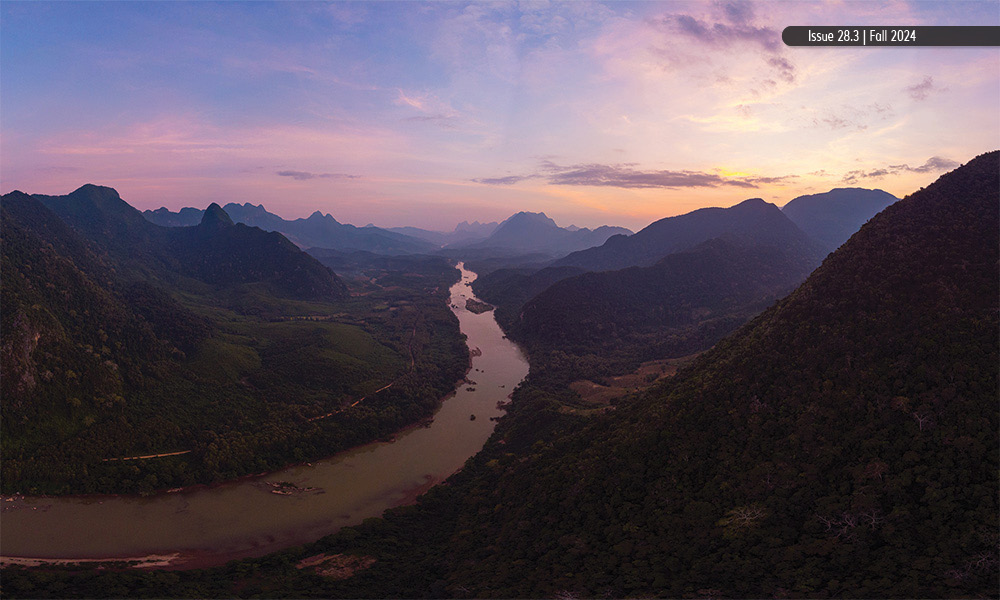 A valley with a winding river and surrounding, tree-covered mountains.