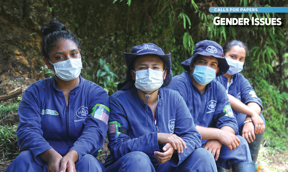 Four female deminers wearing masks sit and pose for a picture.