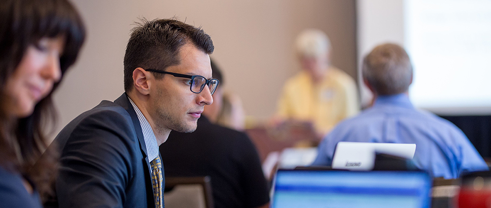A male MBA student with glasses looks studiously at his laptop