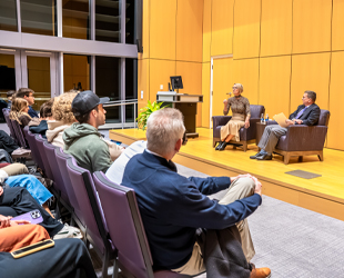 A panel discussion between Lynne Zaledonis ('92) and Dean Mike Busing in a well-lit auditorium with an audience listening intently.