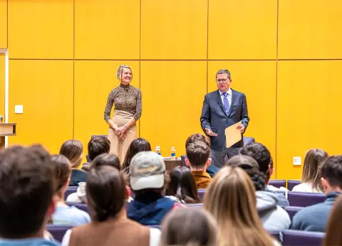 Lynne Zaledonis and Michael Busing stand on stage in Forum, in front of a crowd of students.