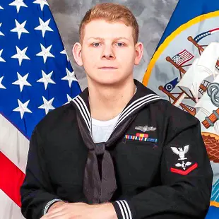 A portrait of U.S. Navy sailor, Austin Ledergerber, in uniform, posed in front of the American flag and the Navy emblem.