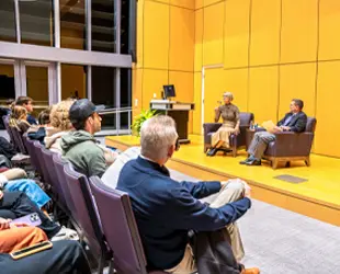 A panel discussion between Lynne Zaledonis ('92) and Dean Mike Busing in a well-lit auditorium with an audience listening intently.