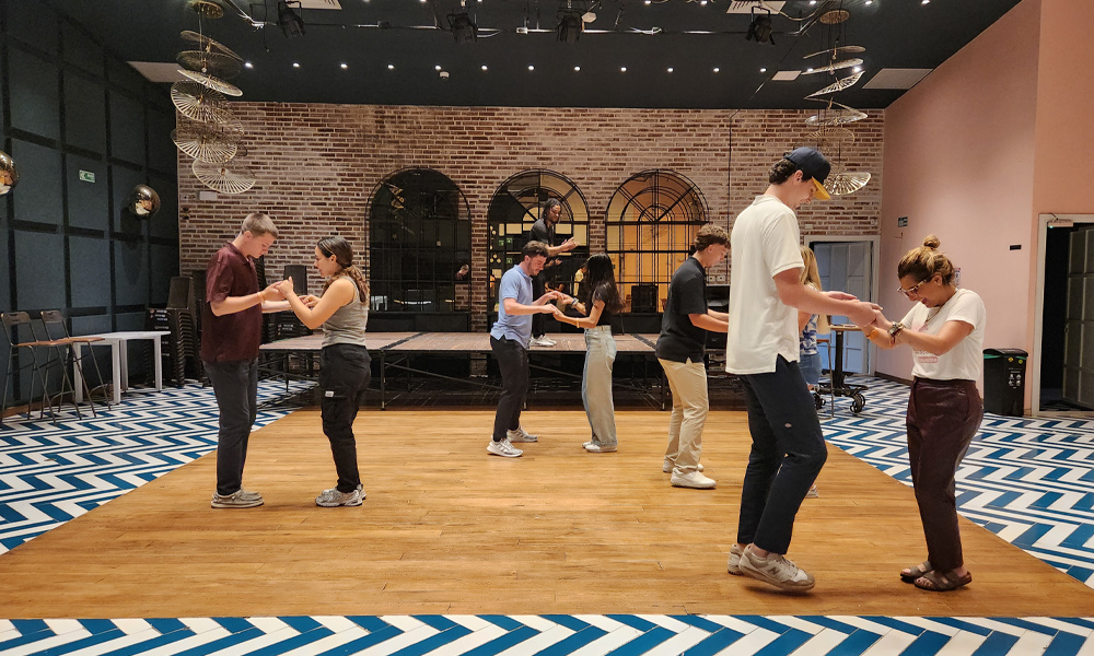 4 couples are on a dance floor, holding hands and practicing. 