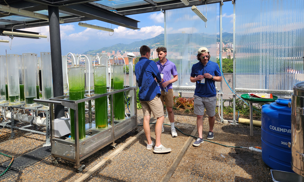 Three men are surrounding by a green liquid in large tubes at an open-air laboratory.