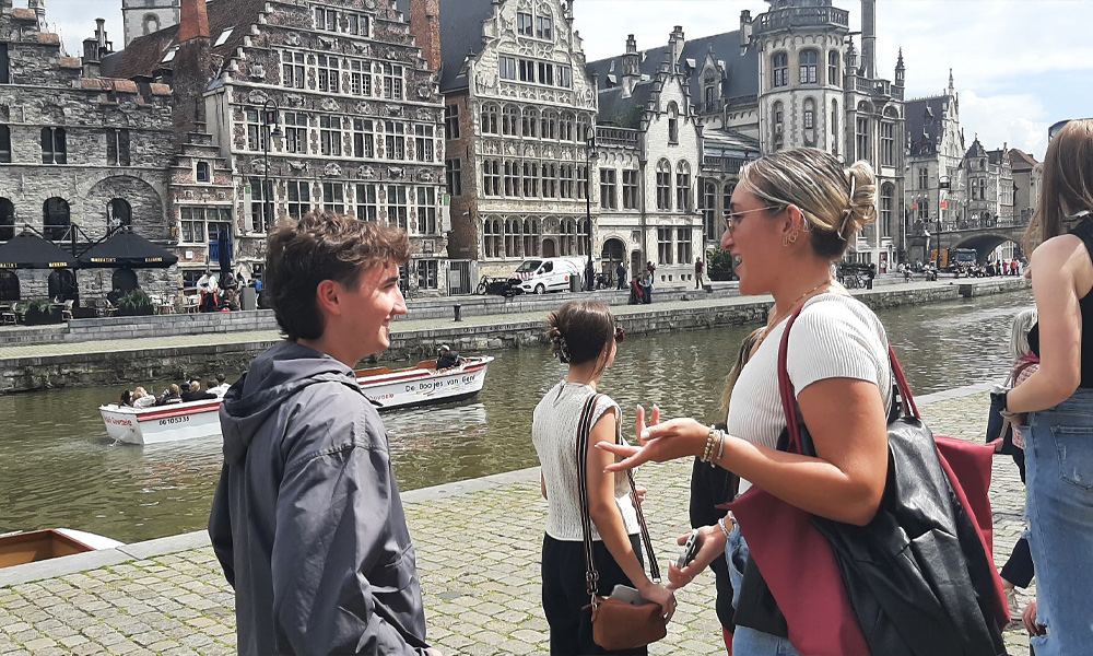 Students chat together in front of historical buildings and the rive in Ghent, Belgium.