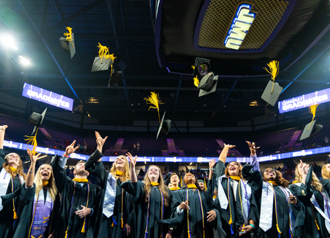 Graduates celebrating and tossing their caps in the air during a graduation ceremony.