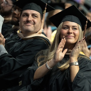 Graduates celebrating at a commencement ceremony, clapping and smiling as they share the moment.