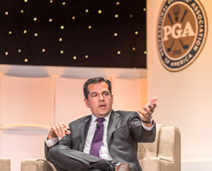 Derek Sprague sits on a stage during a PGA event, with the PGA logo displayed in the background.