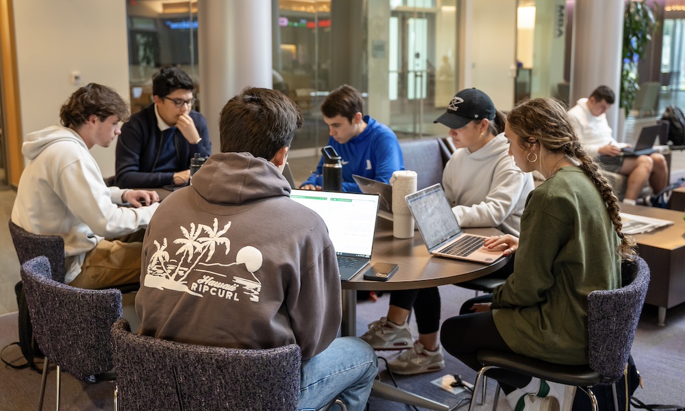 A group of students sitting in the Hartman Hall lobby at a large round table. 