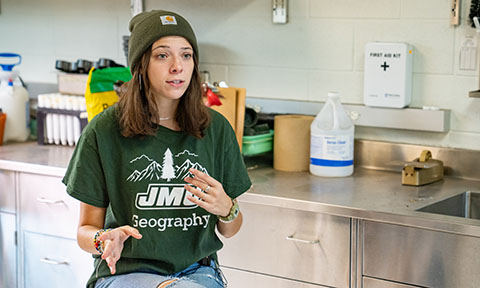 Student sitting on stool in a lab gesturing with her hands