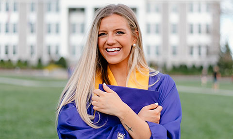 Portrait of a student in grad attire in front of a campus building