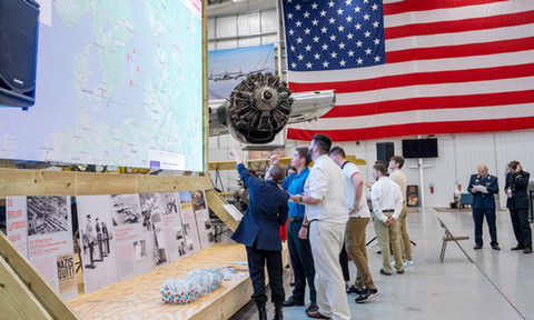 Students and professors working together in front of a huge display in an airplain hangar.