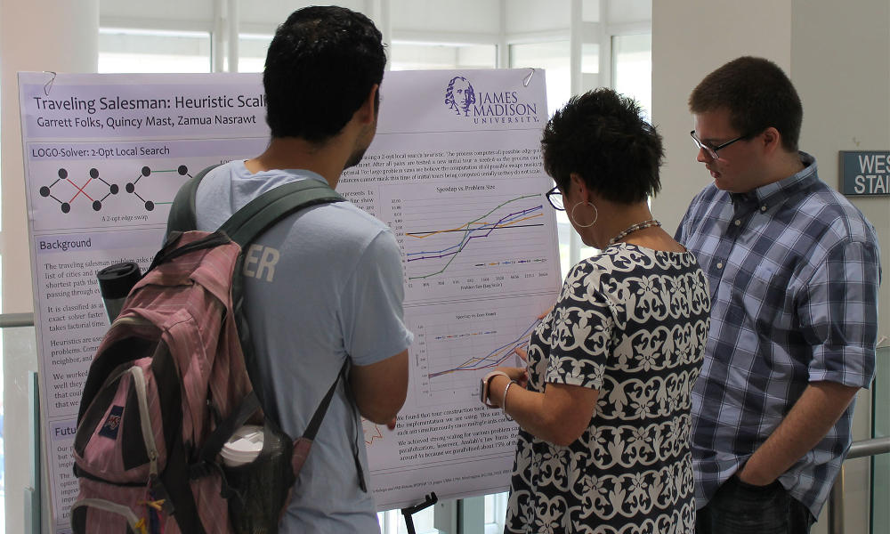 Three people with backs to the camera face a poster, with Sharon Simmons pointing at a spot on the poster.