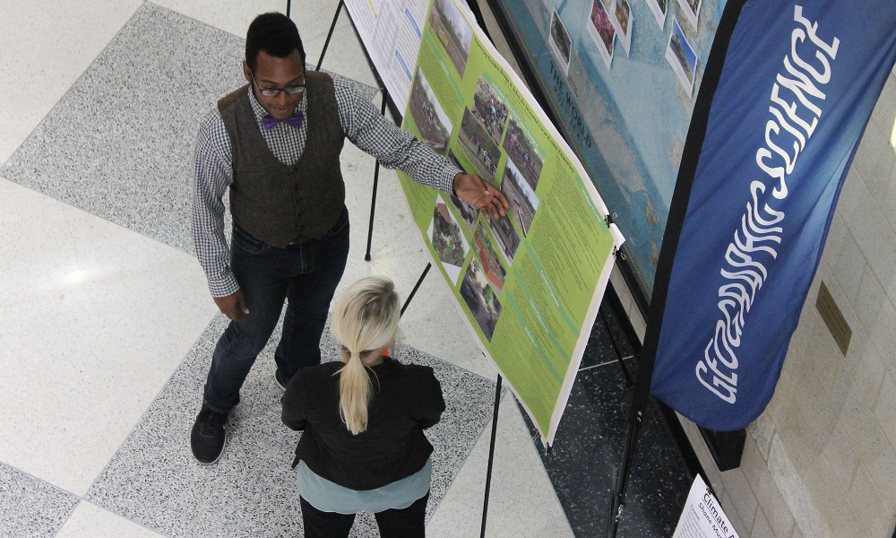 photo taken from the second floor looking down at two people discussing a poster on the first floor.