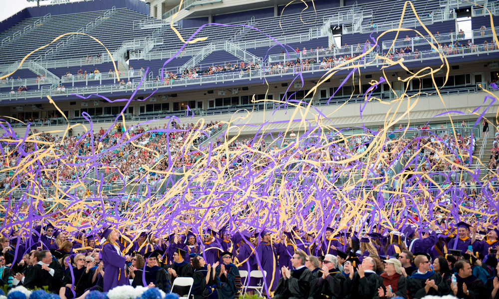 Class of 2014 graduates throw purple and gold streamers in celebration.