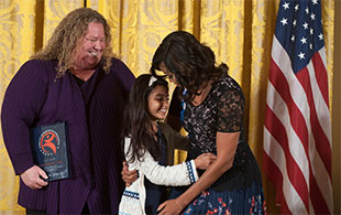 Kim Hartzler-Weakley looks on as Sarah Hussein gets a hug from Micelle Obama.