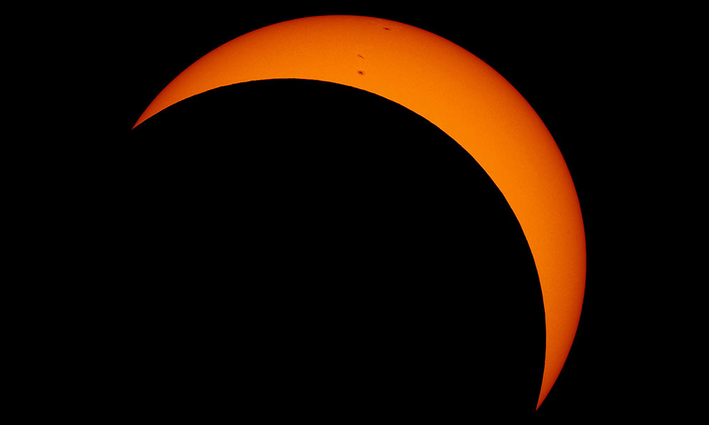 photo of an eclipse showing an orange sun mostly covered by the dark disc of the moon.
