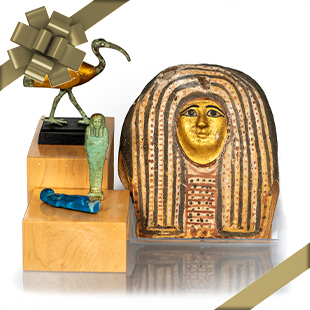 A collection of three ancient Egyptian artifacts, including a golden-faced sarcophagus lid, a blue ceramic piece, and a bird sculpture, all displayed with a decorative bow.