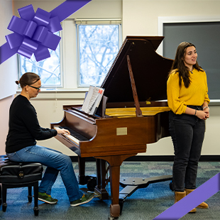 A woman plays the piano while another woman sings, both engaged in a musical performance.