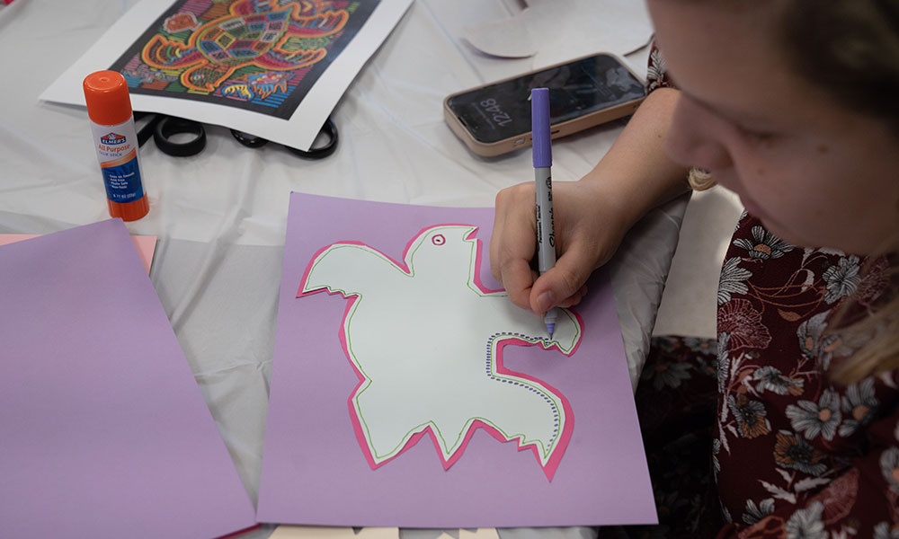 A person works on a craft at a table