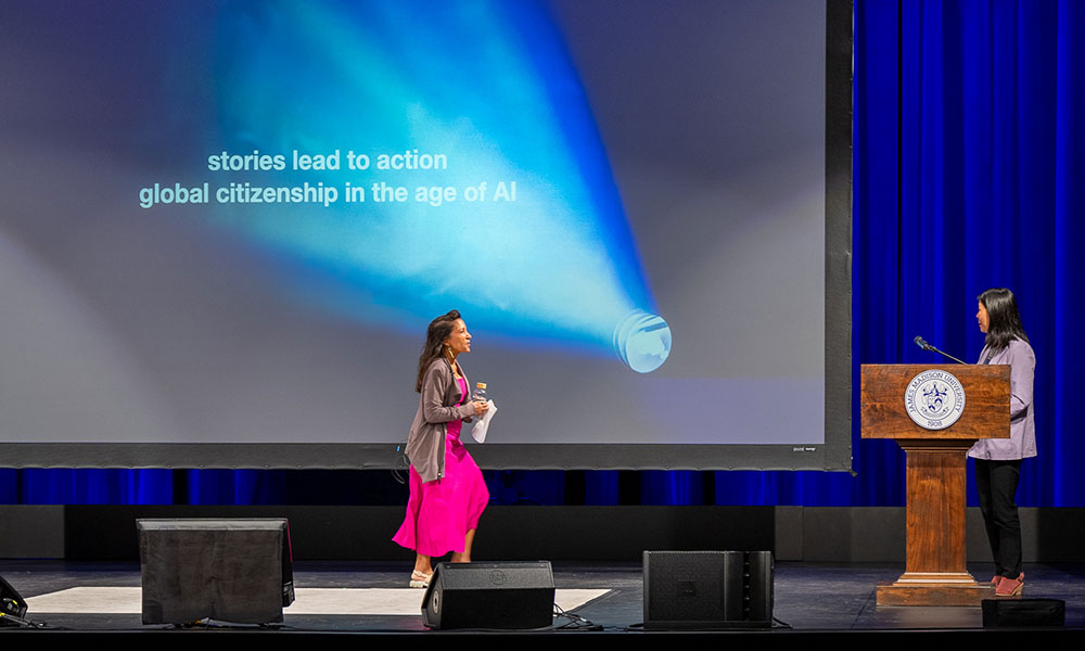 A woman walks across a stage to greet another