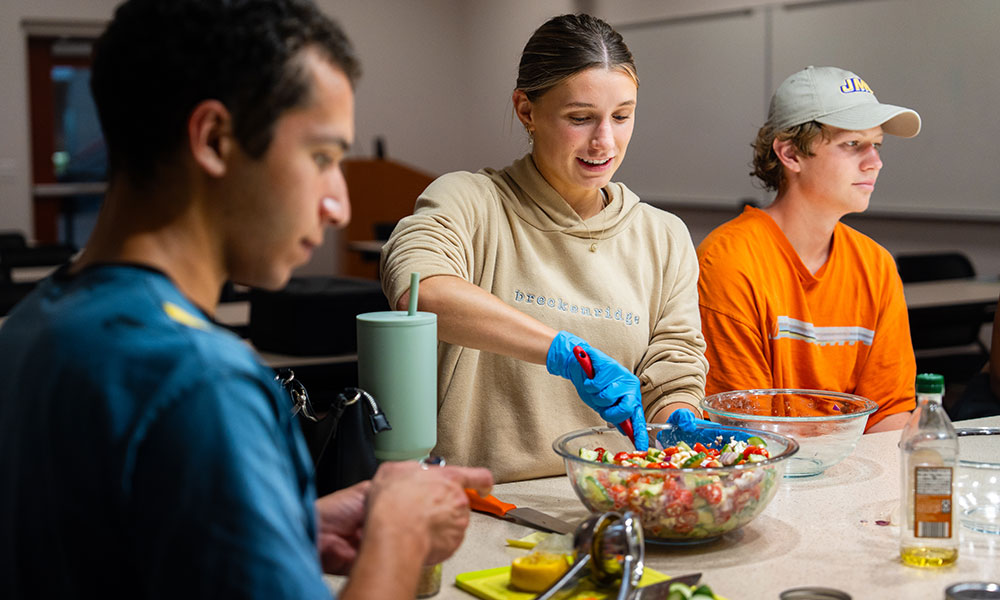 Three students sit at a counter with food they are making