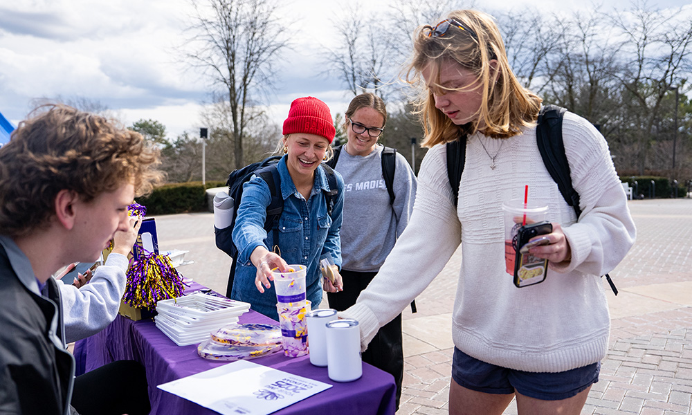 Students who drive themselves outdoors at a table, enjoy snacks and drinks during an event.