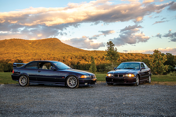 Two BMW cars parked outdoors against a backdrop of mountains and a colorful sunset.