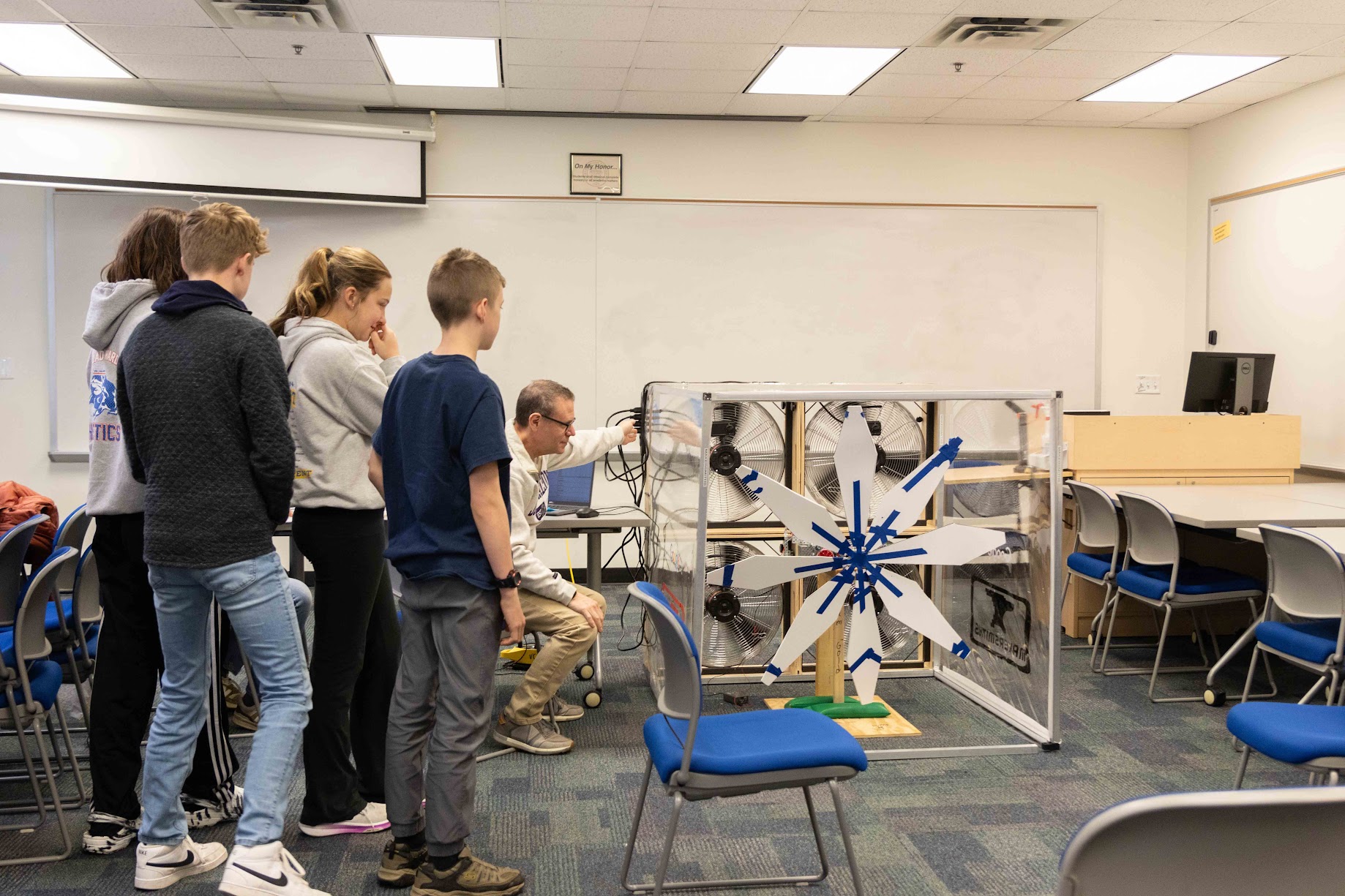 group of students next to a man operating a wind tunnel with a model turbine in it