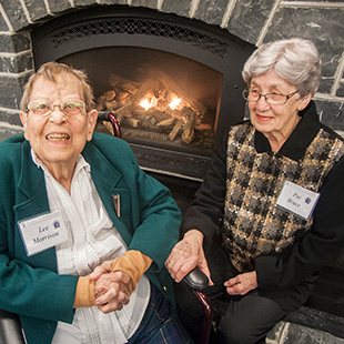 Dr. Lee Morrison and Dr. Pat Bruce sit together at a fireplace at the 10 year anniversary celebration of the MBC.