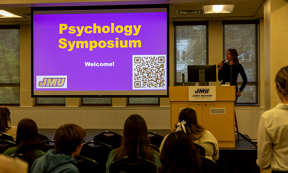 Projector displays "Psychology Symposium" while students and attendees look on.