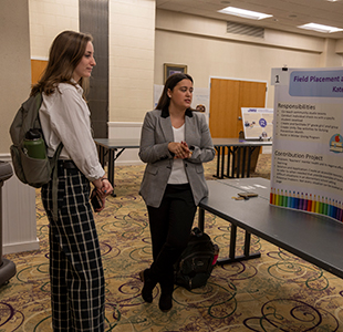 A psychology student discusses her Field Placement poster with a symposium attendee.