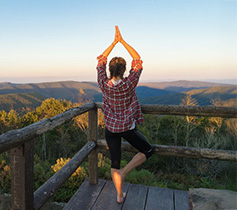 A female college student doing yoga with a mountainous view in the background